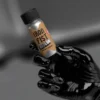 Iron Fist Raw Poppers - Sleek metallic bottle of "Iron Fist Raw" held at an angle by hand wearing black latex glove, dramatic lighting highlights the wood-grain label and silver finish against dark background.