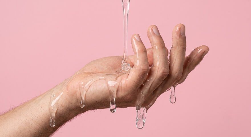 Lubricant pouring onto hand against a pink background.